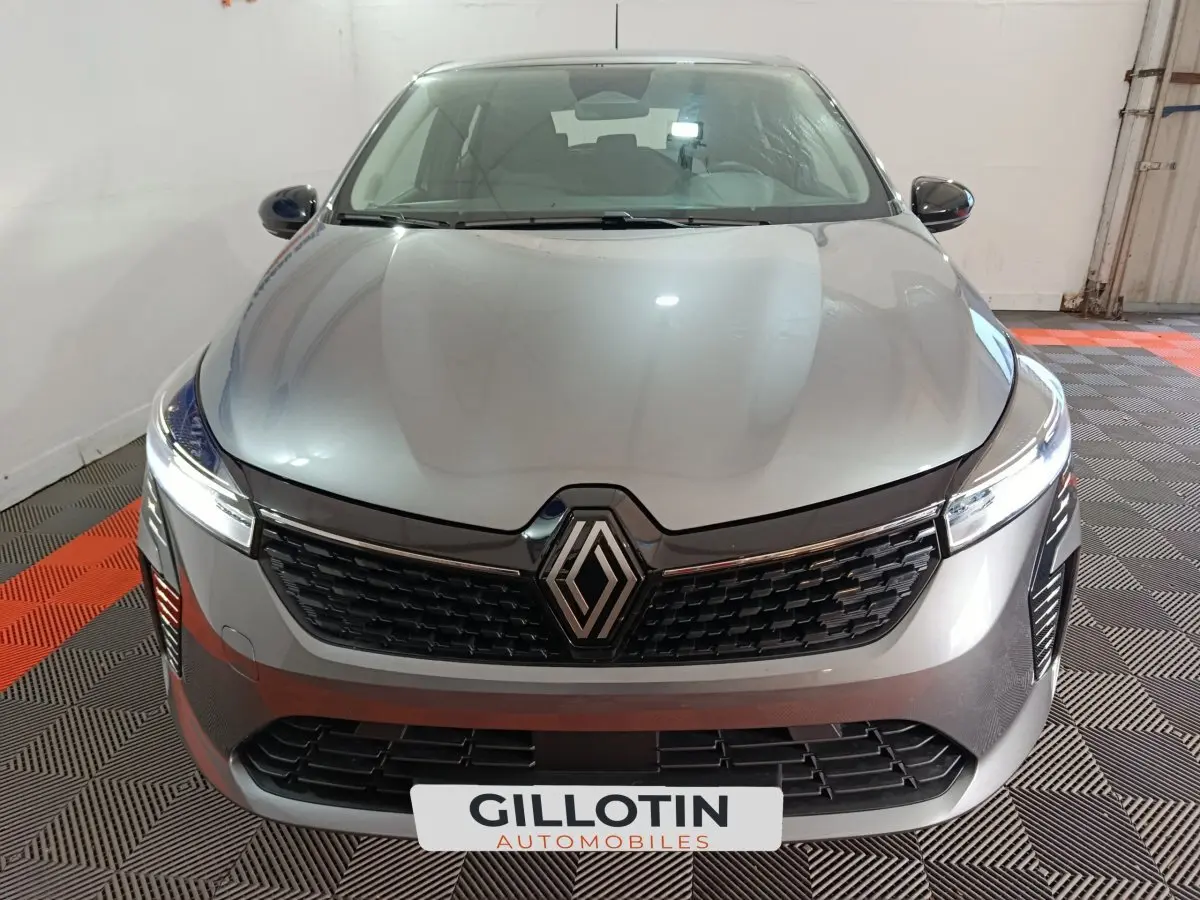 Vue avant rapprochée d'une Renault Clio gris clair avec calandre noire et phares LED allumés dans un garage.