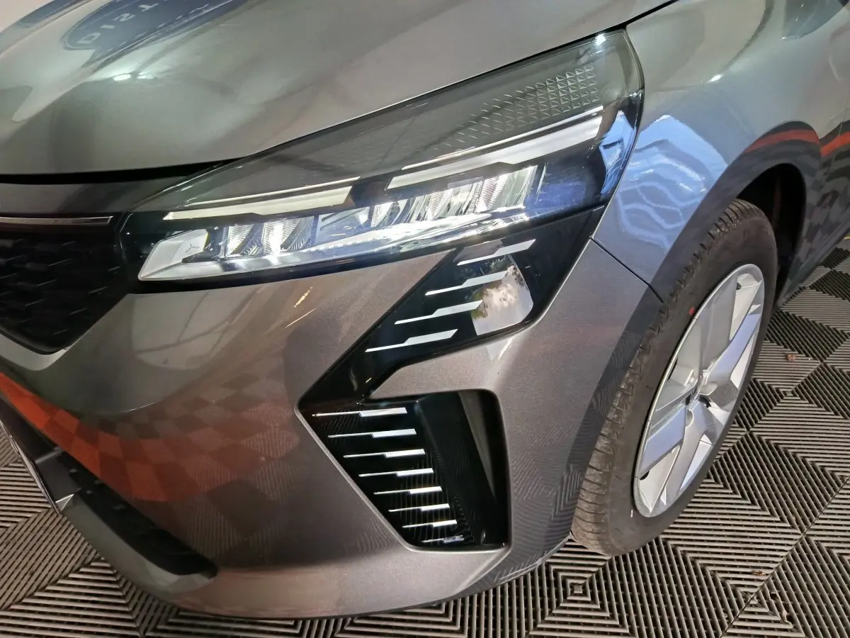 Gros plan sur l'avant droit de la Renault Clio gris clair 2025, mettant en valeur son phare LED et la jante moderne.