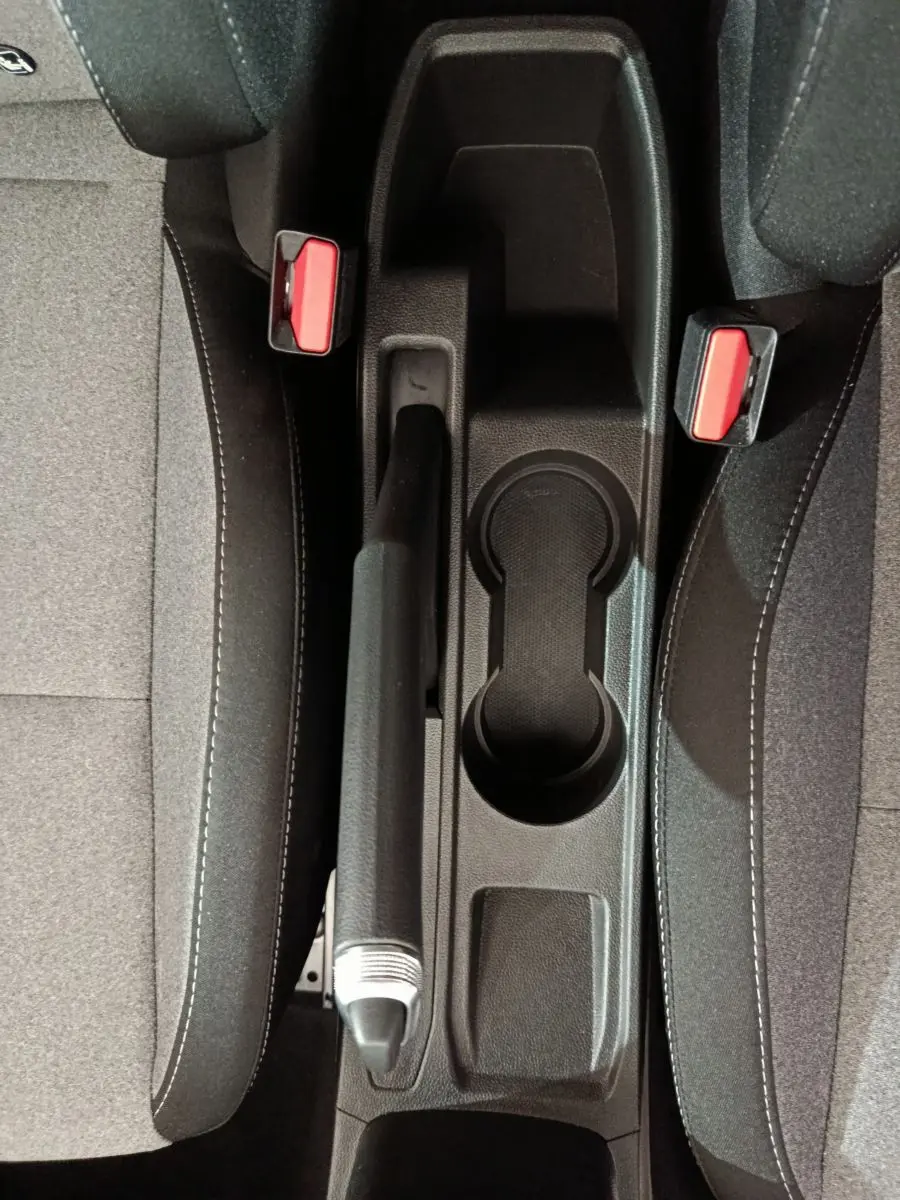 Vue plongeante sur la console centrale noire entre les sièges gris clair de la Renault Clio Evolution 2025, avec frein à main et porte-gobelets.