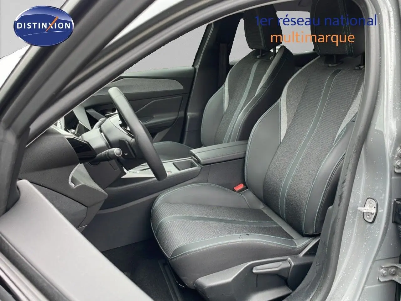 Vue intérieure côté conducteur de la Peugeot 408 2025 gris selenium, sièges tissu et cuir avec coutures contrastées.