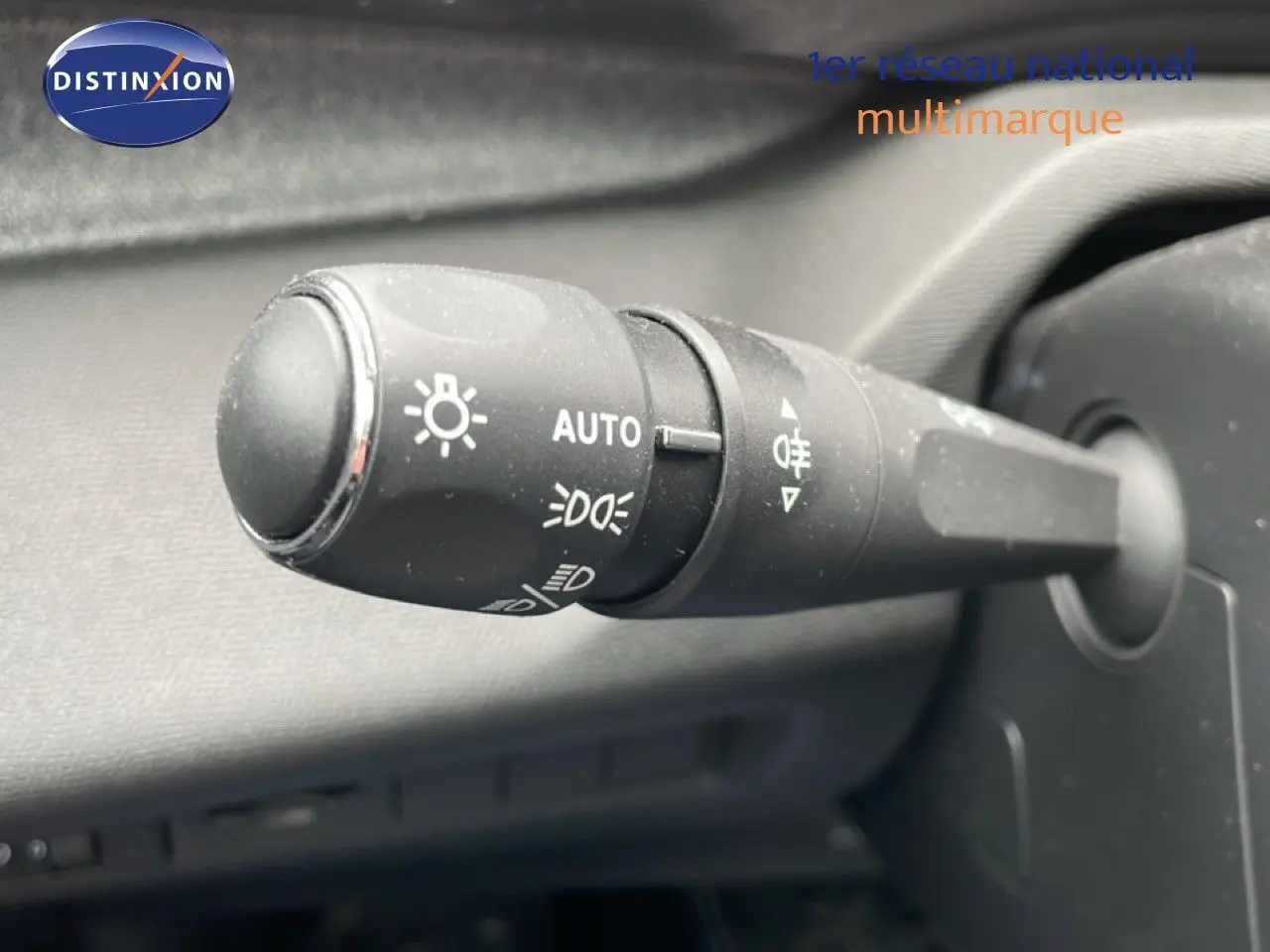 Gros plan sur la commande des phares du Peugeot 408 1.2 Hybrid 145ch, bouton noir avec symboles lumineux blancs.