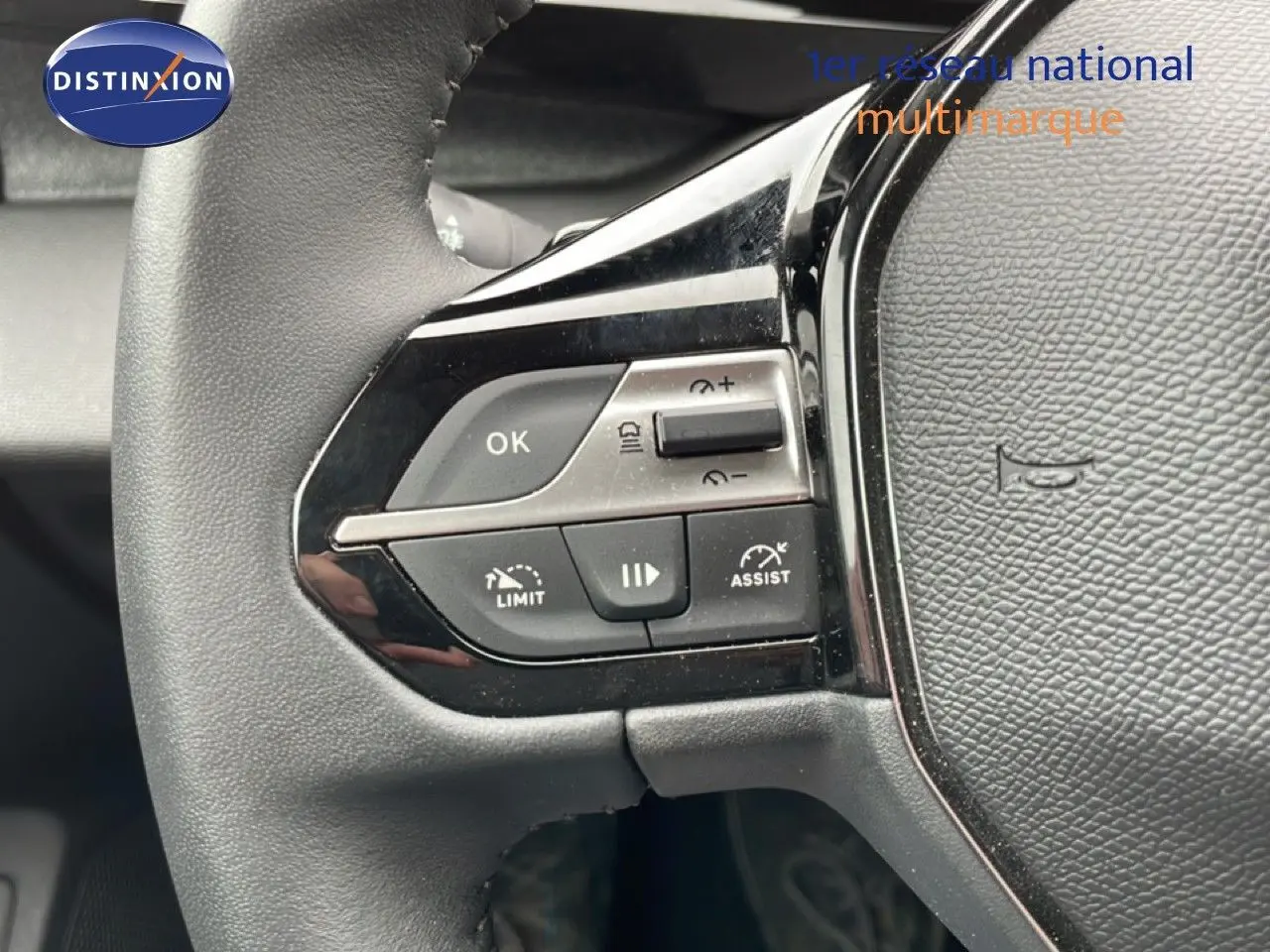 Gros plan sur les commandes à gauche du volant noir du Peugeot 408 1.2 Hybrid 2025, boutons de limitation et assistances visibles.
