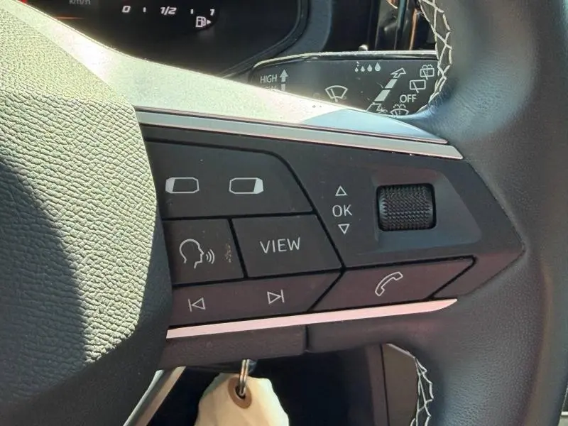 Gros plan sur les commandes multifonctions du volant cuir noir du SEAT Arona 2025, avec surpiqûres blanches visibles.