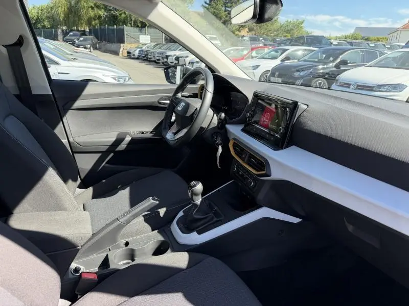 Intérieur côté conducteur du SEAT Arona 2025, tableau de bord noir et blanc avec écran tactile et volant cuir multifonction.
