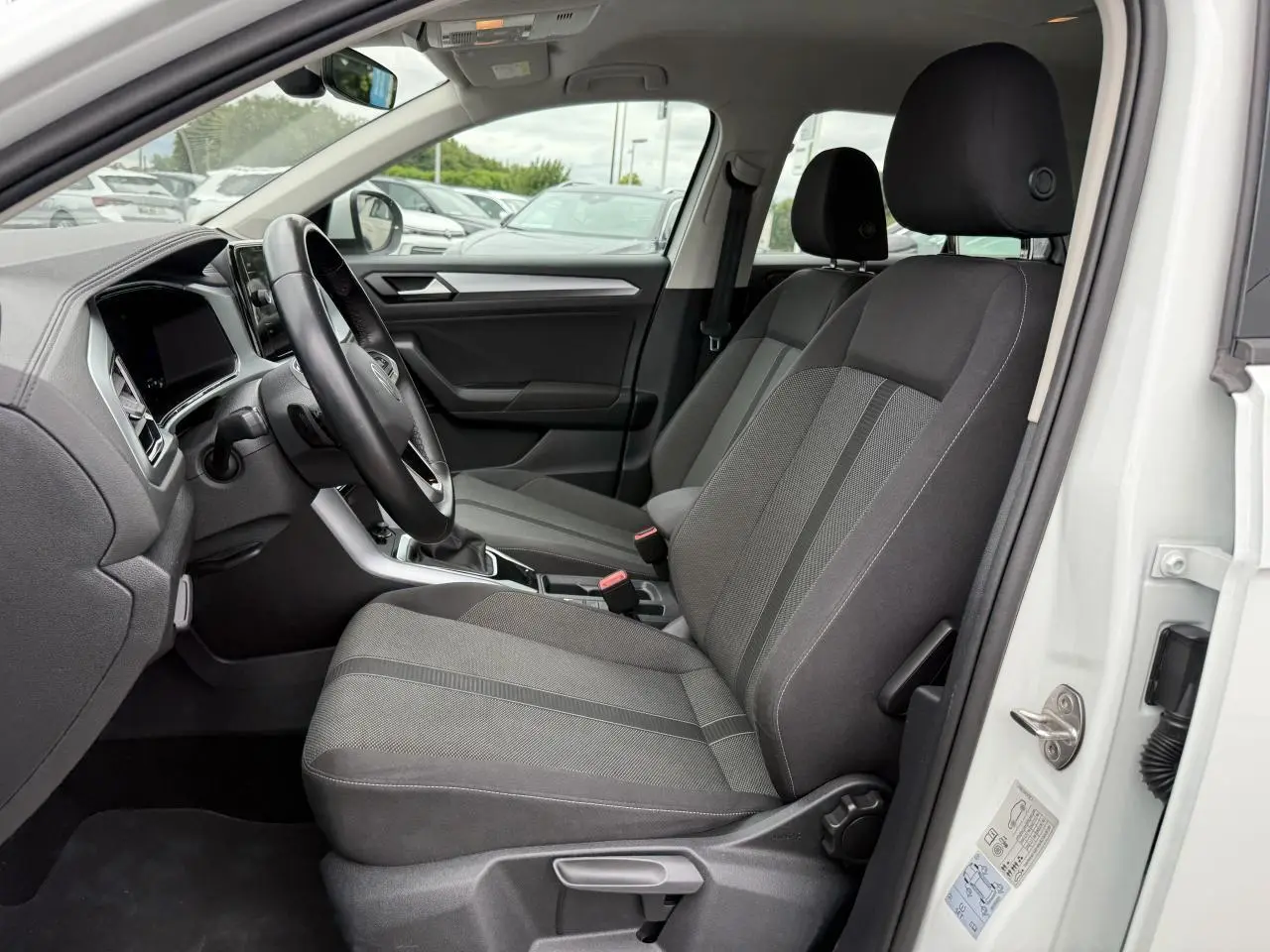 Vue intérieure côté conducteur du Volkswagen T-Roc blanc pur 2022, sièges tissu gris et tableau de bord moderne.