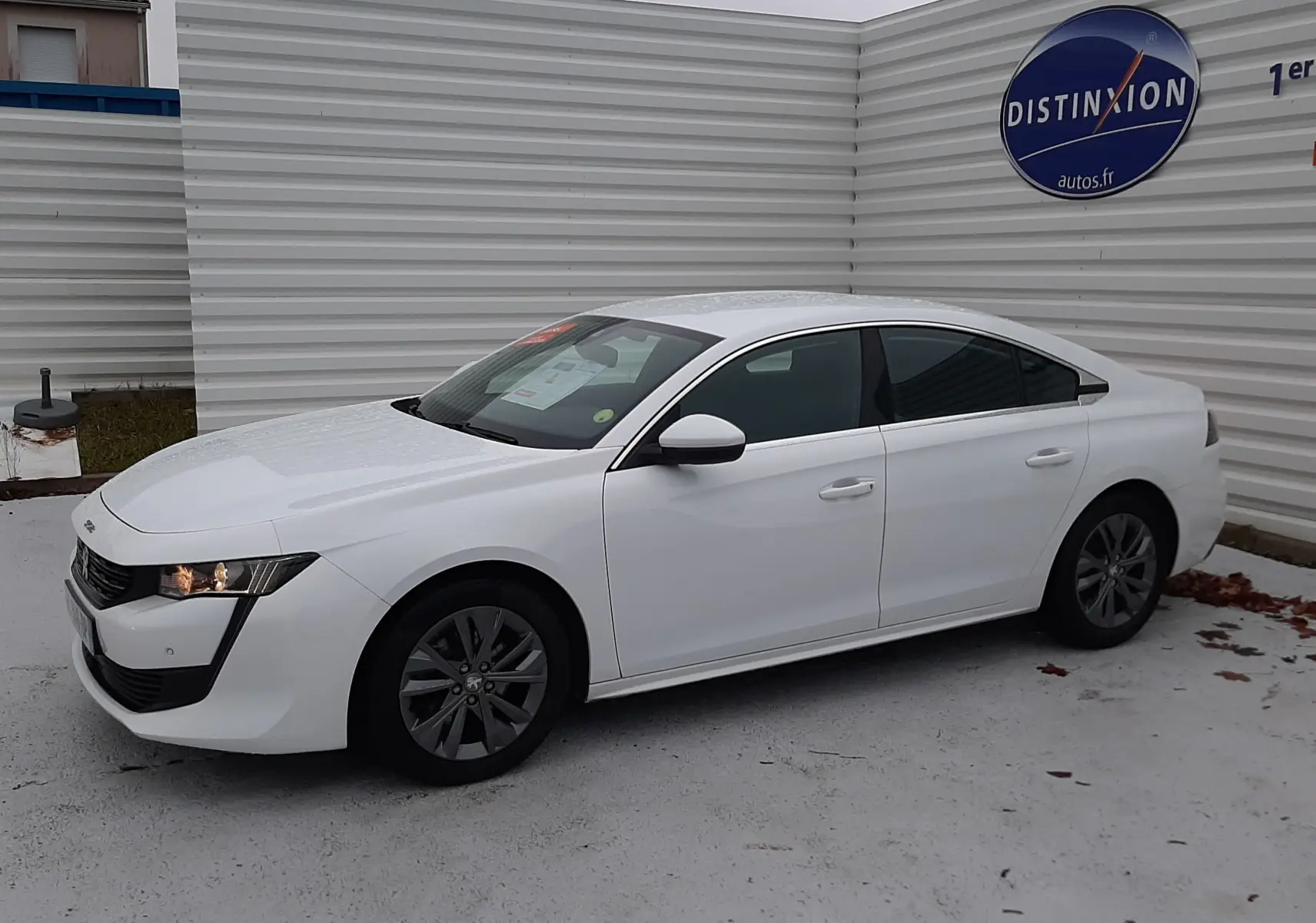 Peugeot 508 blanc vue de profil côté gauche, avec feux avant allumés et jantes foncées, stationnée devant un mur blanc.