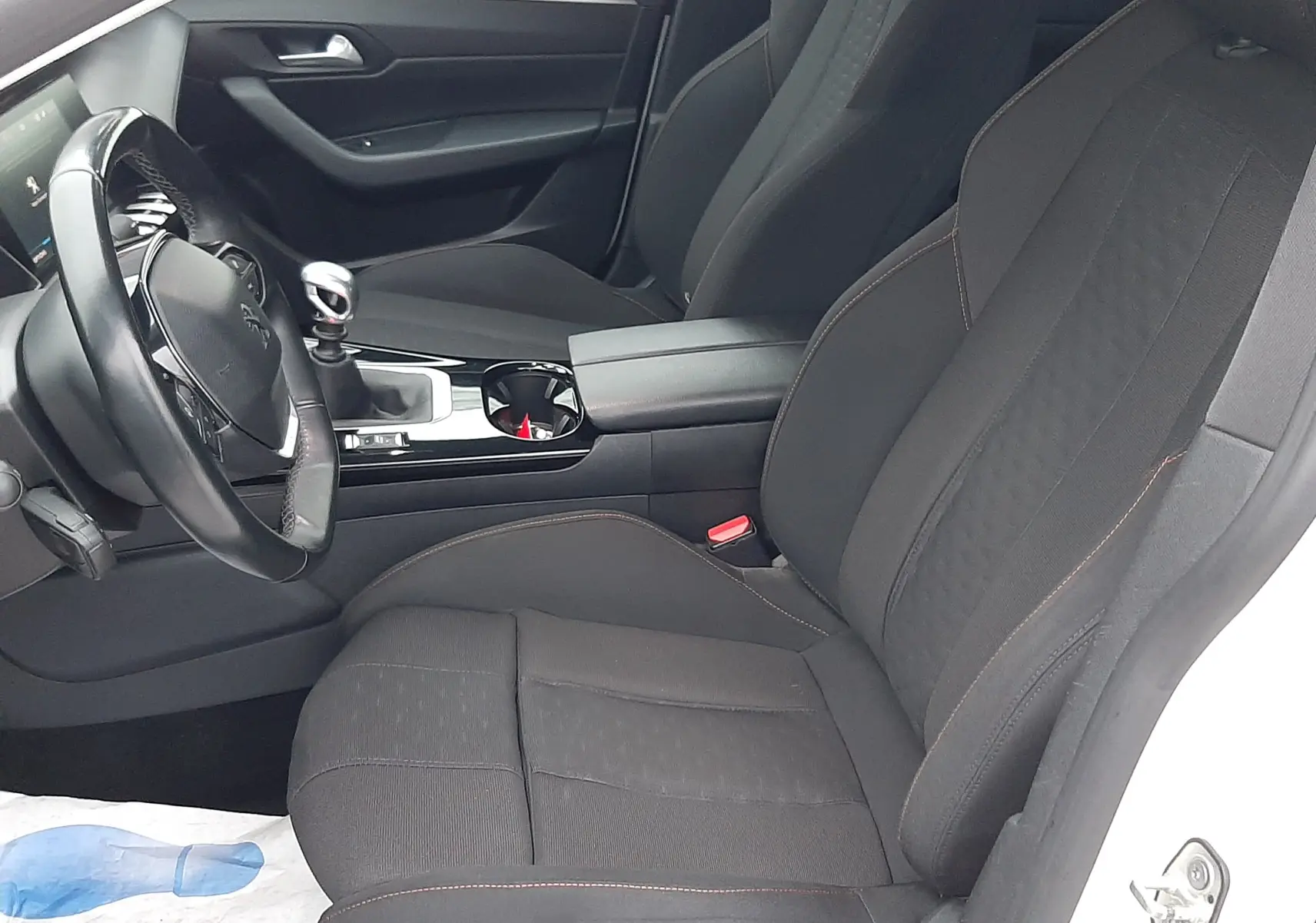Vue intérieure côté conducteur de la Peugeot 508 blanche, montrant les sièges noirs et la console centrale avec levier de vitesse manuel.