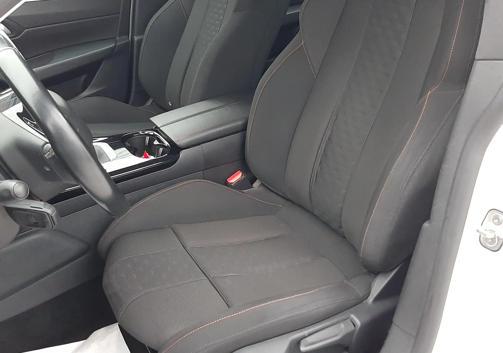 Vue intérieure côté conducteur de la Peugeot 508 blanche de 2018, sièges noirs avec surpiqûres rouges et console centrale brillante.