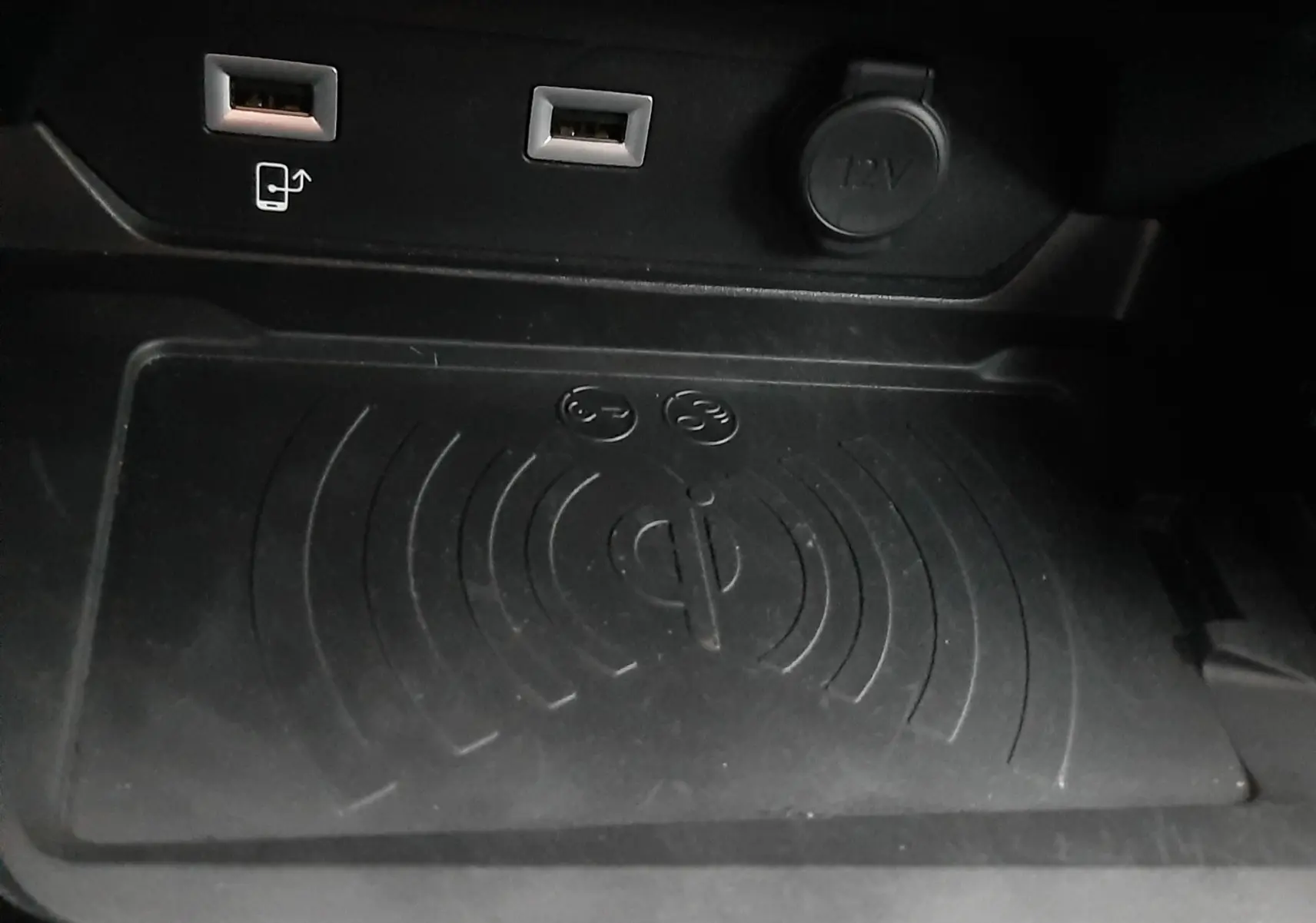 Gros plan sur la console centrale noire de la Peugeot 508 blanche, montrant les ports USB, prise 12V et zone de recharge sans fil Qi.