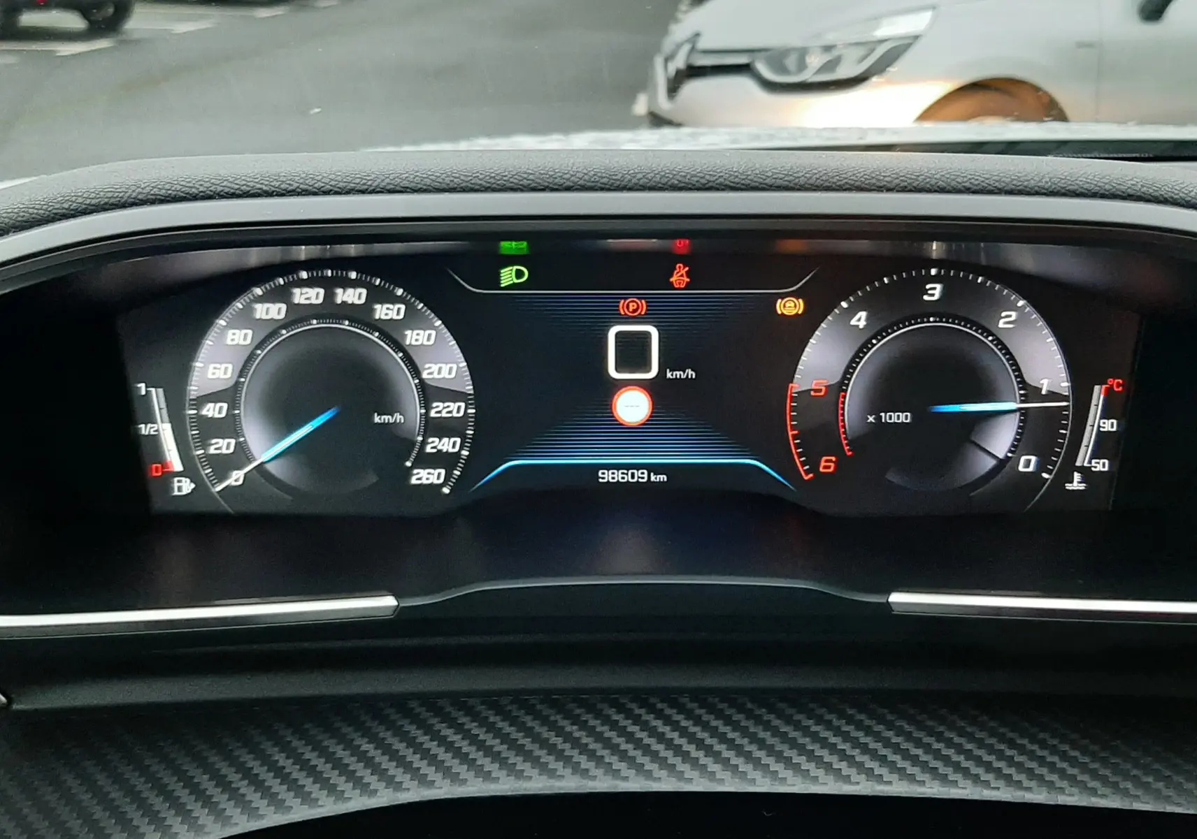 Tableau de bord numérique de Peugeot 508 blanc, affichant vitesse, compte-tours et témoins lumineux, vue intérieure frontale.