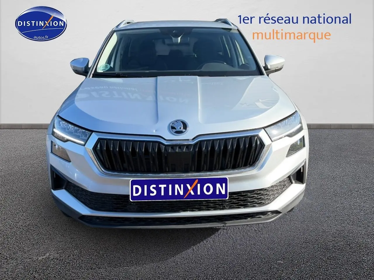 Vue avant d'un Skoda Karoq gris 2025 avec calandre noire et phares LED, sur fond neutre avec logo Distinxion.