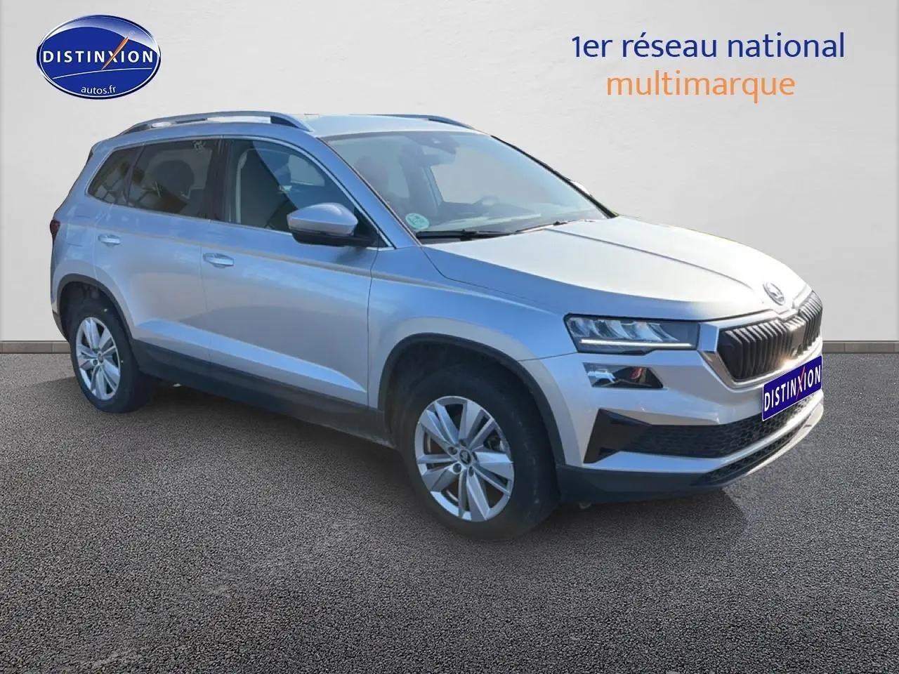 Vue 3/4 avant gauche d'un Skoda Karoq gris 2025 avec jantes alu et barres de toit visibles.