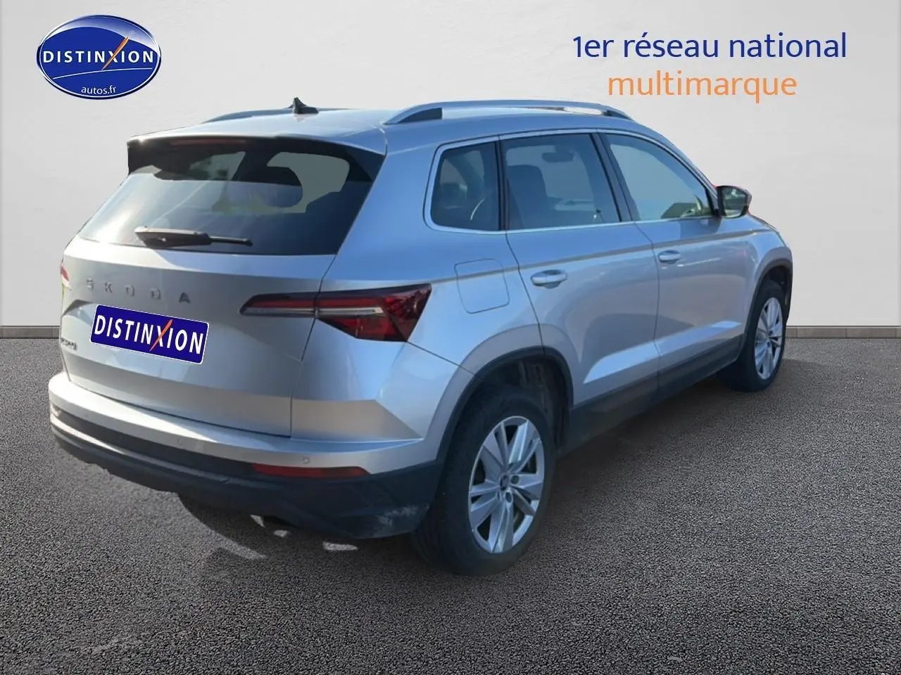 Vue 3/4 arrière droite d'un Skoda Karoq gris 2025 avec barres de toit et feux arrière LED visibles.