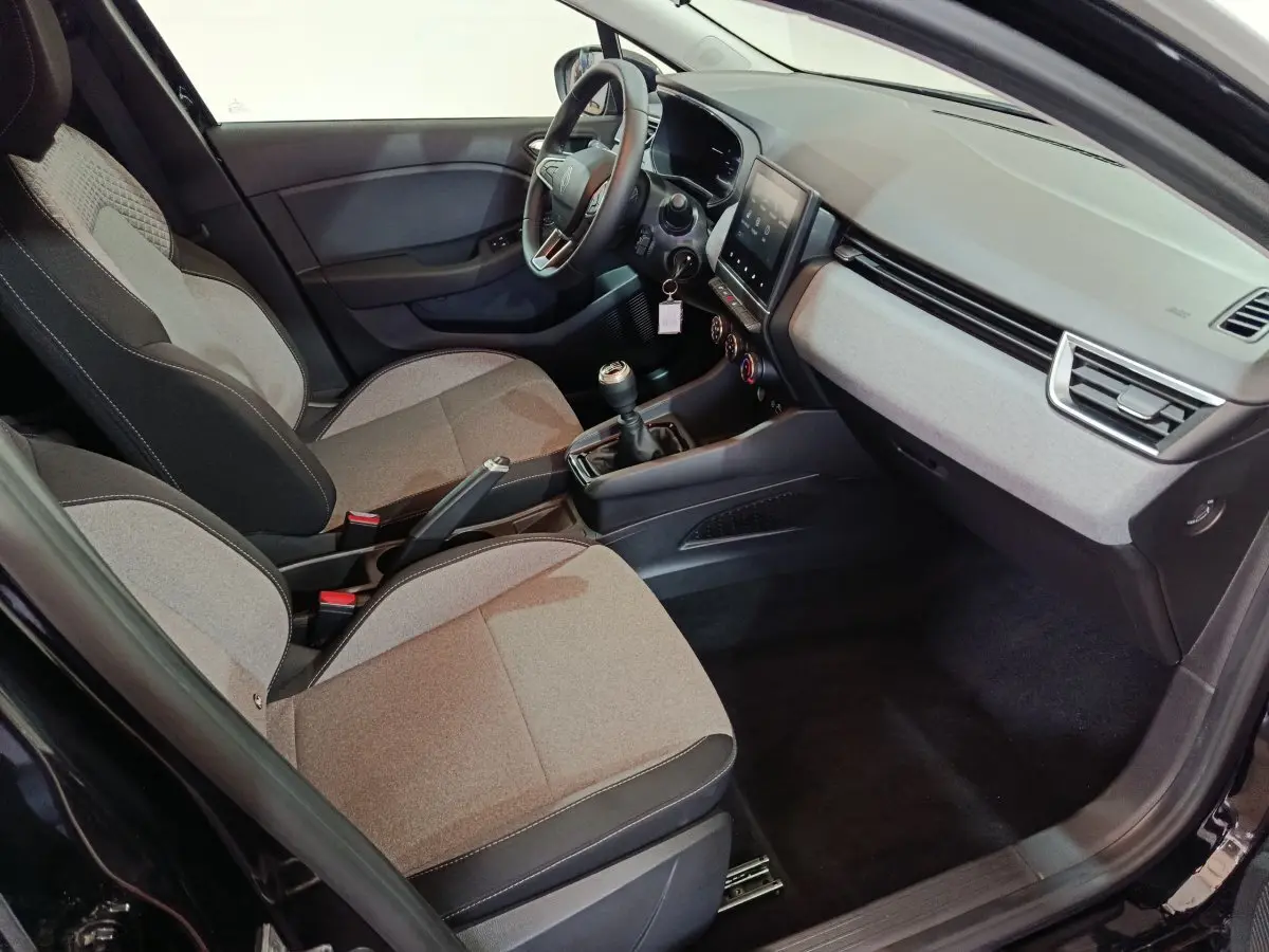 Vue intérieure côté conducteur de la Renault Clio noire 2025, montrant sièges tissu, volant multifonctions et écran tactile central.