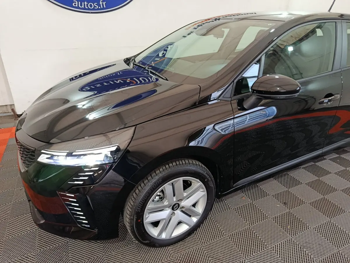 Vue 3/4 avant gauche de la Renault Clio noire 2025 avec phares LED allumés et jantes argentées.