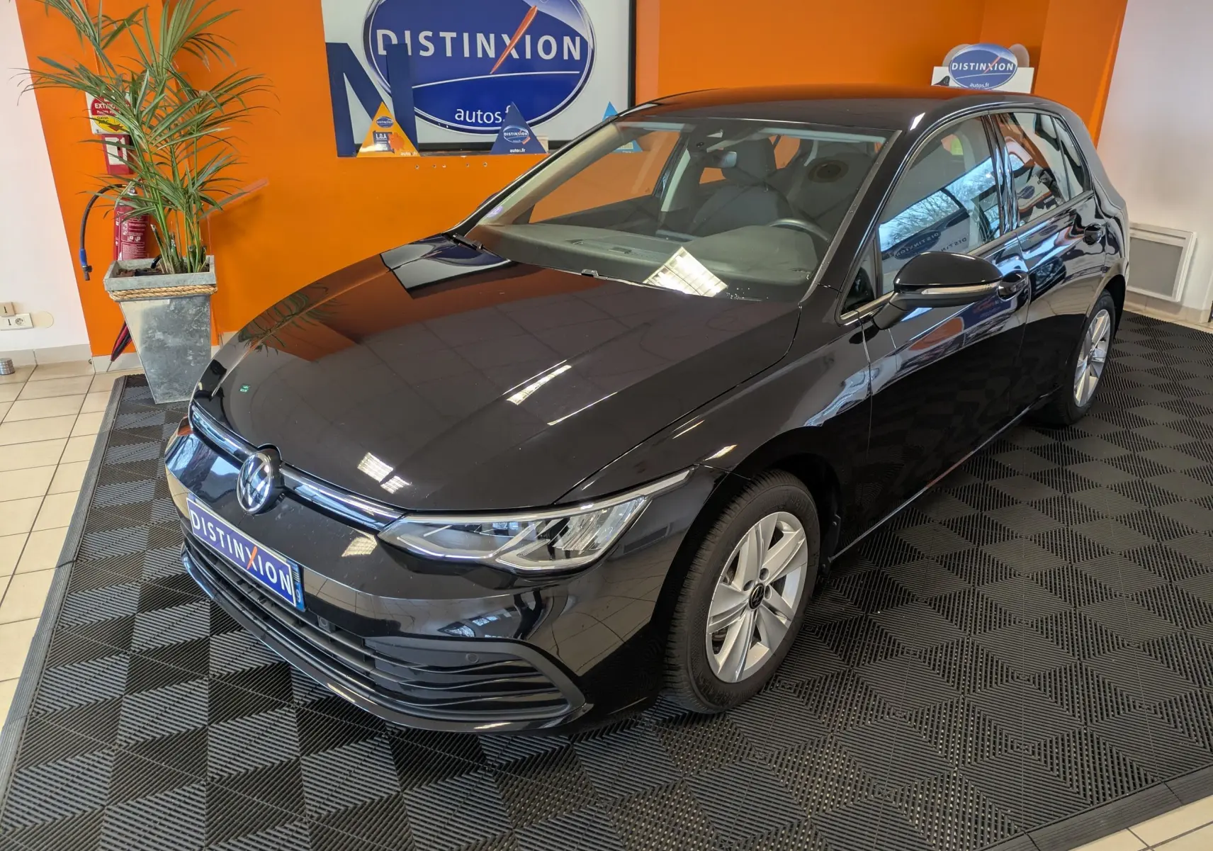 Volkswagen Golf 1.5 eTSI Style noire vue en 3/4 avant droit dans un showroom avec mur orange.