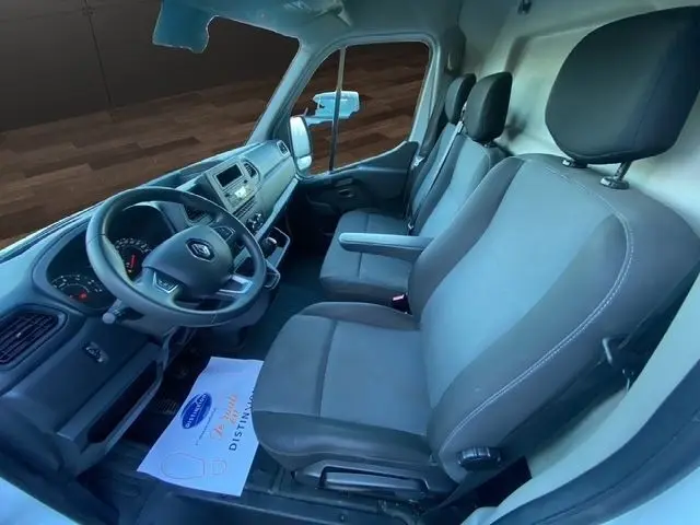 Vue intérieure côté conducteur du Renault Master blanc 2022, montrant les sièges avant et le tableau de bord avec volant multifonction.