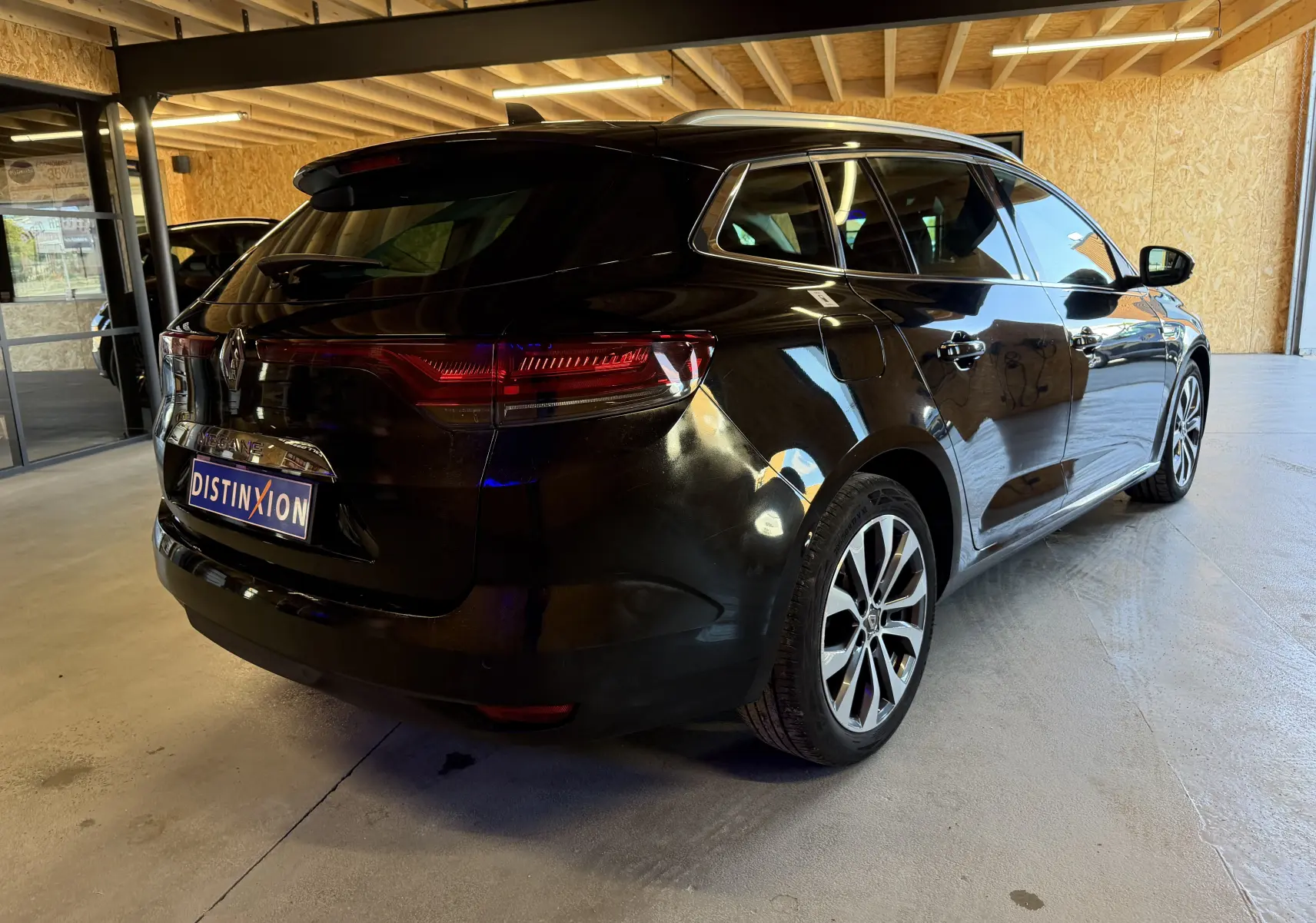Vue 3/4 arrière droite d'une Renault Mégane Estate noire étoilée 2024, stationnée en intérieur avec jantes alliage visibles.