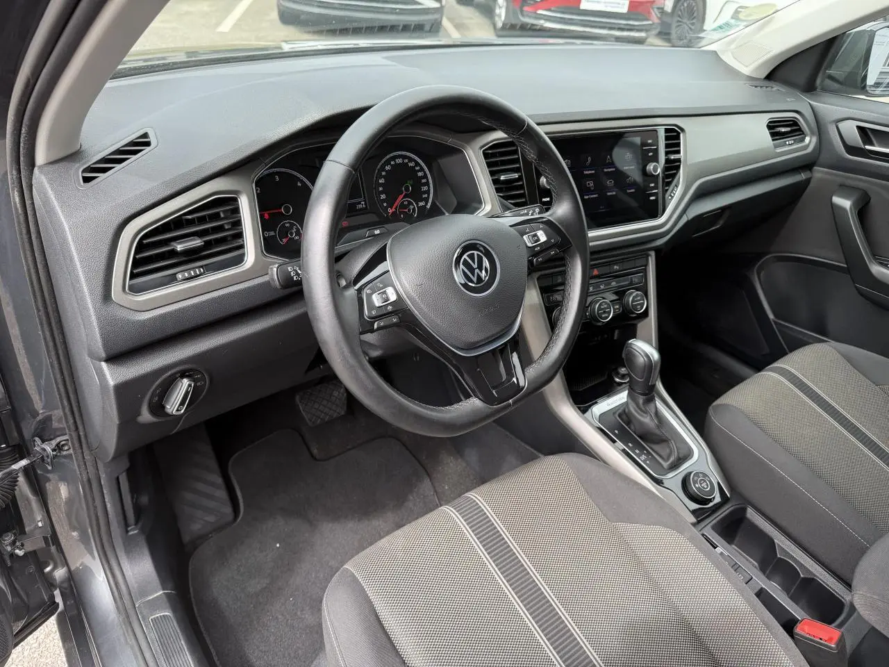Vue intérieure côté conducteur du Volkswagen T-Roc gris Indium, volant cuir multifonction et console centrale avec écran tactile.