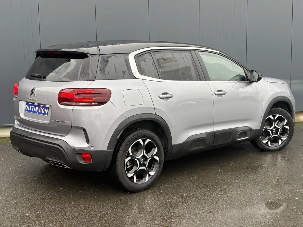 Vue 3/4 arrière droite d'un Citroën C5 Aircross Hybrid gris Artense avec toit noir et jantes alliage 18 pouces.