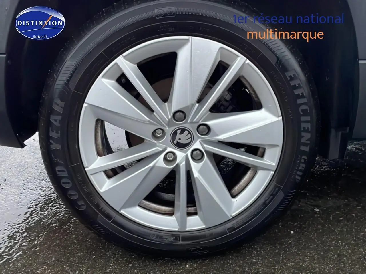 Gros plan sur la jante alu argentée d'une Skoda Karoq blanc glacial, pneu Goodyear visible sur sol humide.