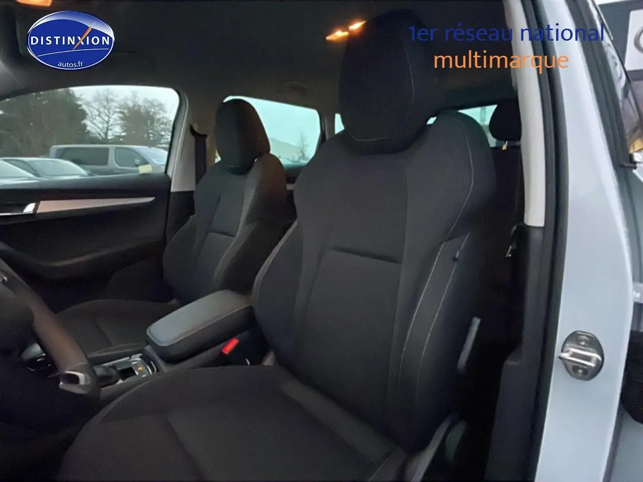 Vue intérieure côté avant droit du Skoda Karoq blanc glacial, mettant en valeur les sièges noirs et l'accoudoir central.