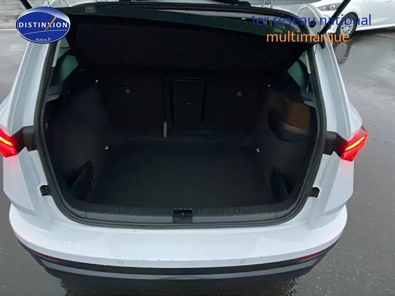 Coffre ouvert vu de l'arrière d'un Skoda Karoq blanc glacial avec feux arrière LED allumés.