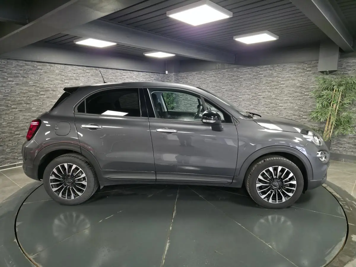 Profil droit d'un Fiat 500X gris 2024 avec jantes alliage 17'' et rétroviseurs noirs dans un showroom.