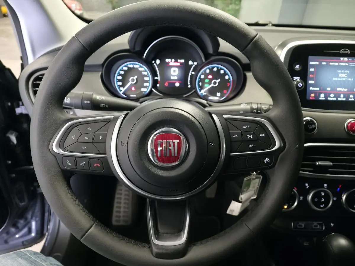 Vue rapprochée du volant noir de la Fiat 500X 2024 avec tableau de bord et écran tactile visible en arrière-plan.