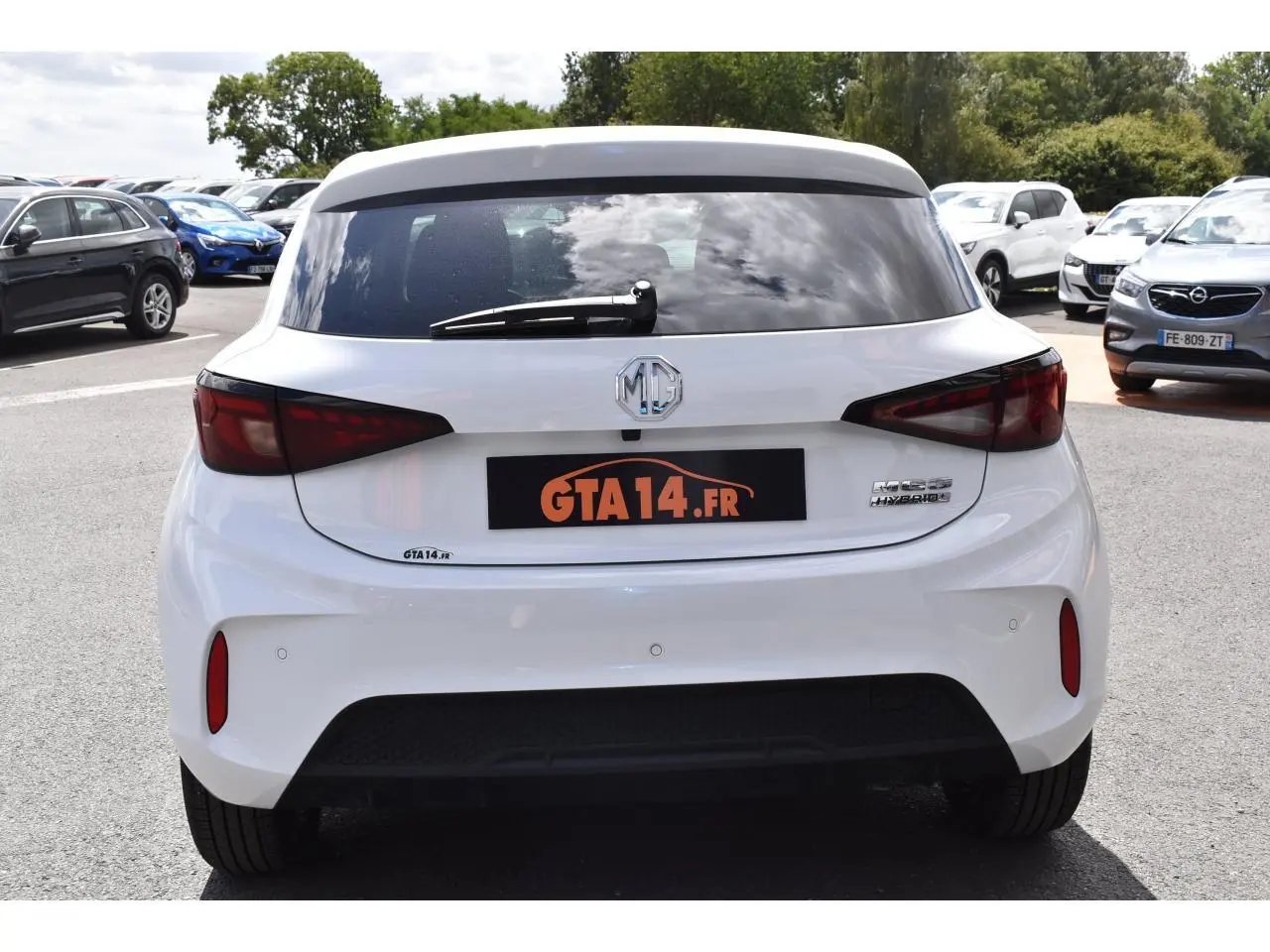 Vue arrière d'une MG3 blanche hybride 2026 avec feux arrière foncés et logo MG visible sur un parking.