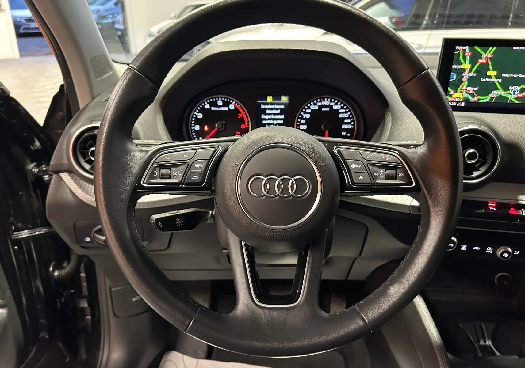 Vue centrée sur le volant cuir noir de l'Audi Q2 2023 avec tableau de bord et écran GPS allumé.