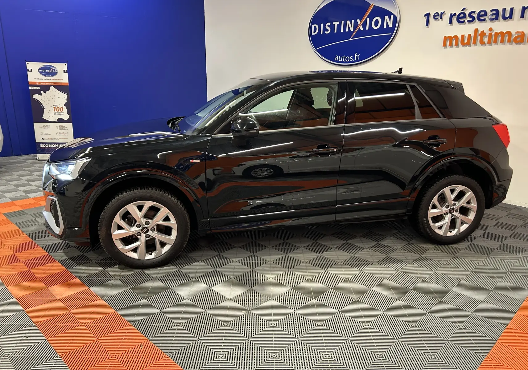 Audi Q2 noir métal vue de profil côté gauche dans un showroom avec jantes argentées et badge S-Line visible.