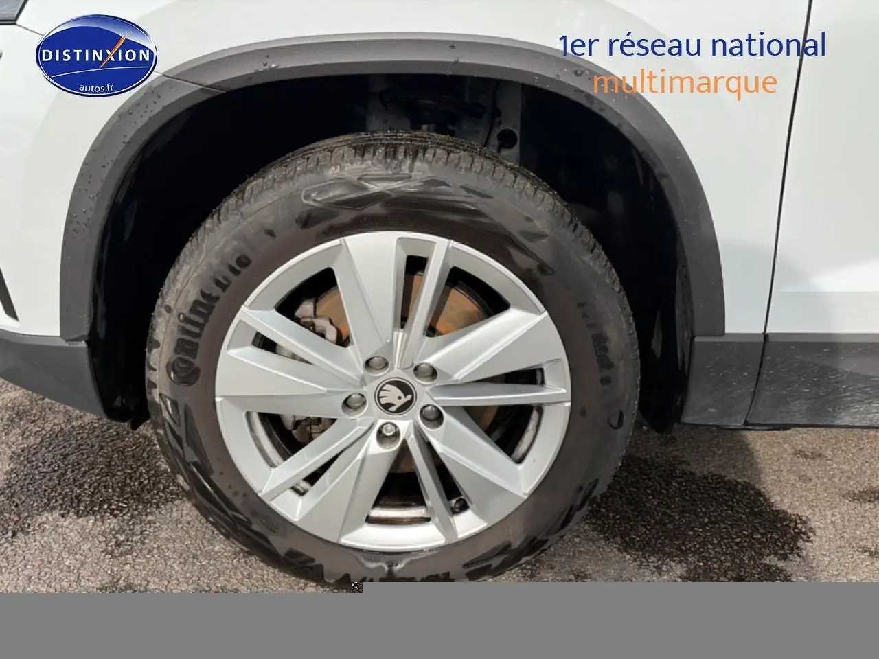 Gros plan sur la roue avant gauche d'un Skoda Karoq blanc glacial avec jante alu et logo Skoda au centre.