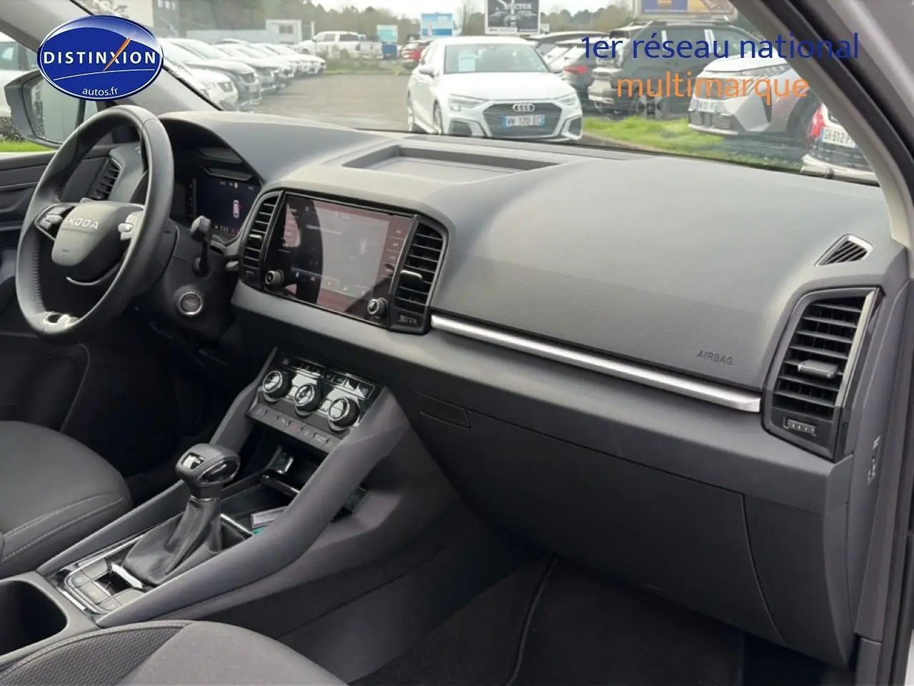 Vue intérieure côté passager du tableau de bord et console centrale du Skoda Karoq blanc glacial, avec écran tactile et volant cuir multifonction.
