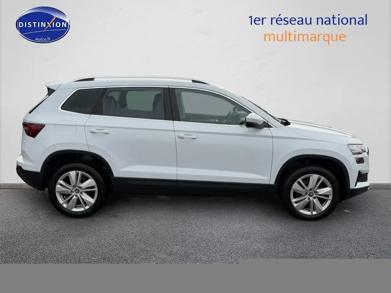 Vue latérale droite d'un Skoda Karoq blanc glacial avec jantes alliage et barres de toit noires.