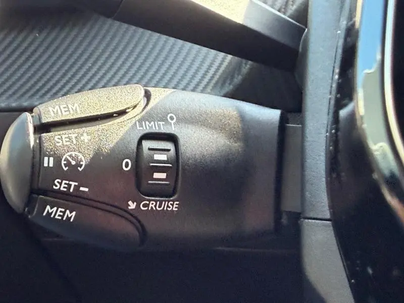 Gros plan sur la commande de régulateur de vitesse de la Peugeot 208 2025, finition Allure, intérieur noir.