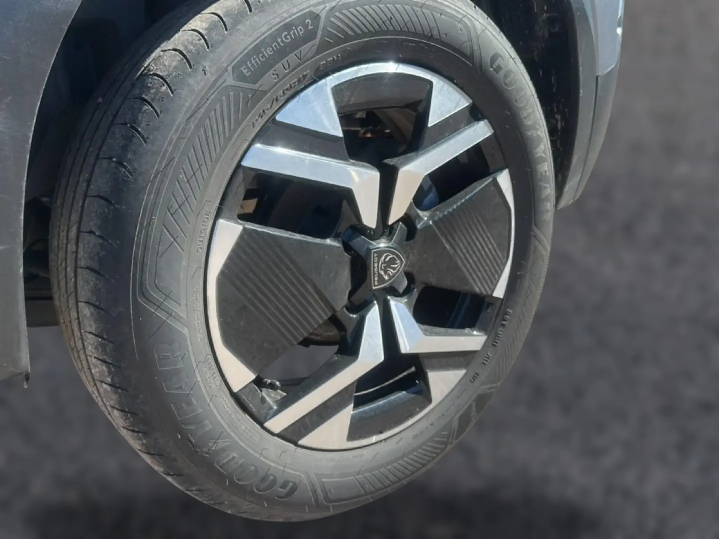 Gros plan sur la roue avant gauche du Peugeot 2008 gris Artense avec jante alu au design moderne et logo central lion.
