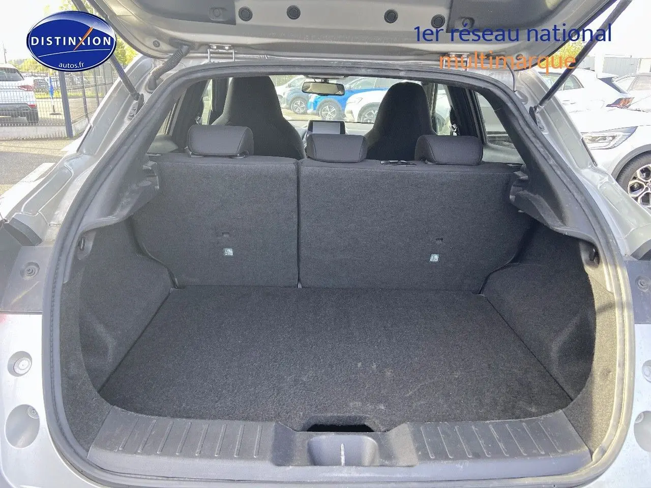 Vue arrière du coffre ouvert d'un Nissan Juke gris clair 2021, montrant l'espace de chargement et les dossiers de sièges arrière relevés.