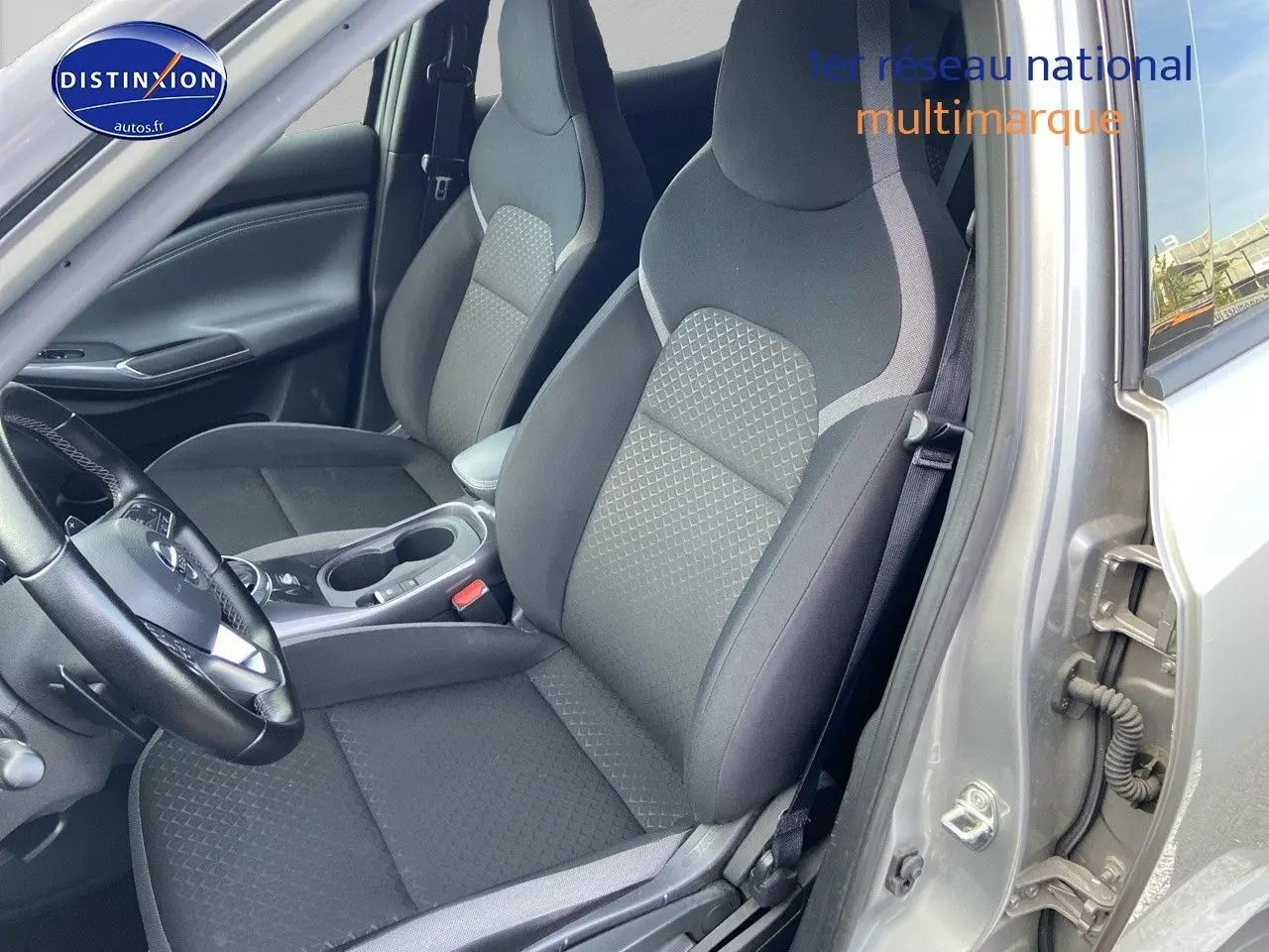 Vue intérieure côté conducteur du Nissan Juke gris clair 2021, mettant en valeur les sièges en tissu noir et la console centrale.