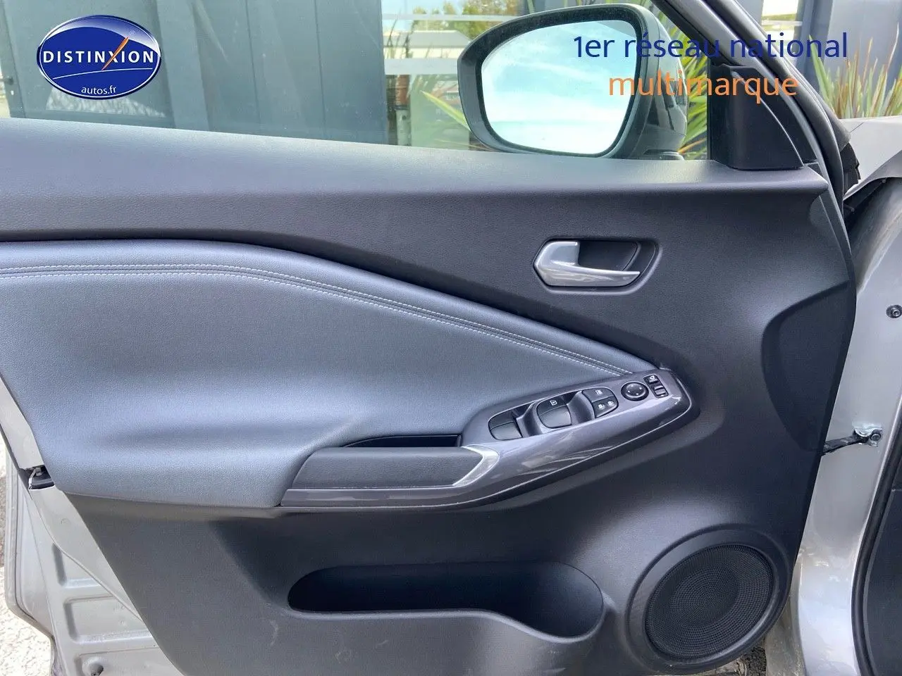 Intérieur de la porte avant gauche du Nissan Juke gris clair 2021, avec commandes électriques et haut-parleur intégré.