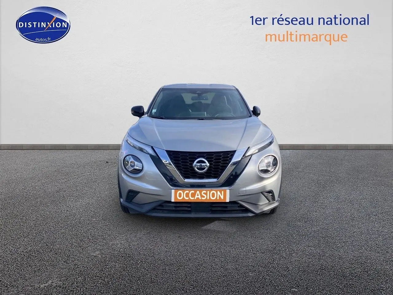Vue de face d'un Nissan Juke gris clair 2021 avec calandre en V chromée et plaque "OCCASION" visible.