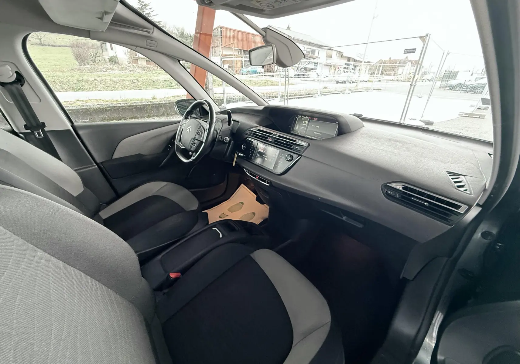 Vue intérieure côté conducteur de la Citroën C4 Picasso 2015, sièges tissu noir et gris, tableau de bord moderne.