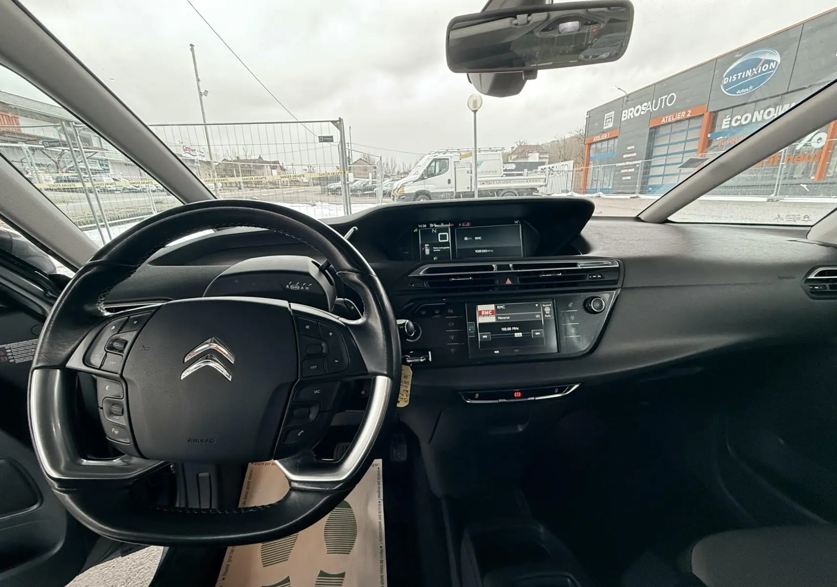 Vue intérieure centrée sur le volant et tableau de bord noir du Citroën C4 Picasso gris platinium, avec écran tactile et commandes au volant.