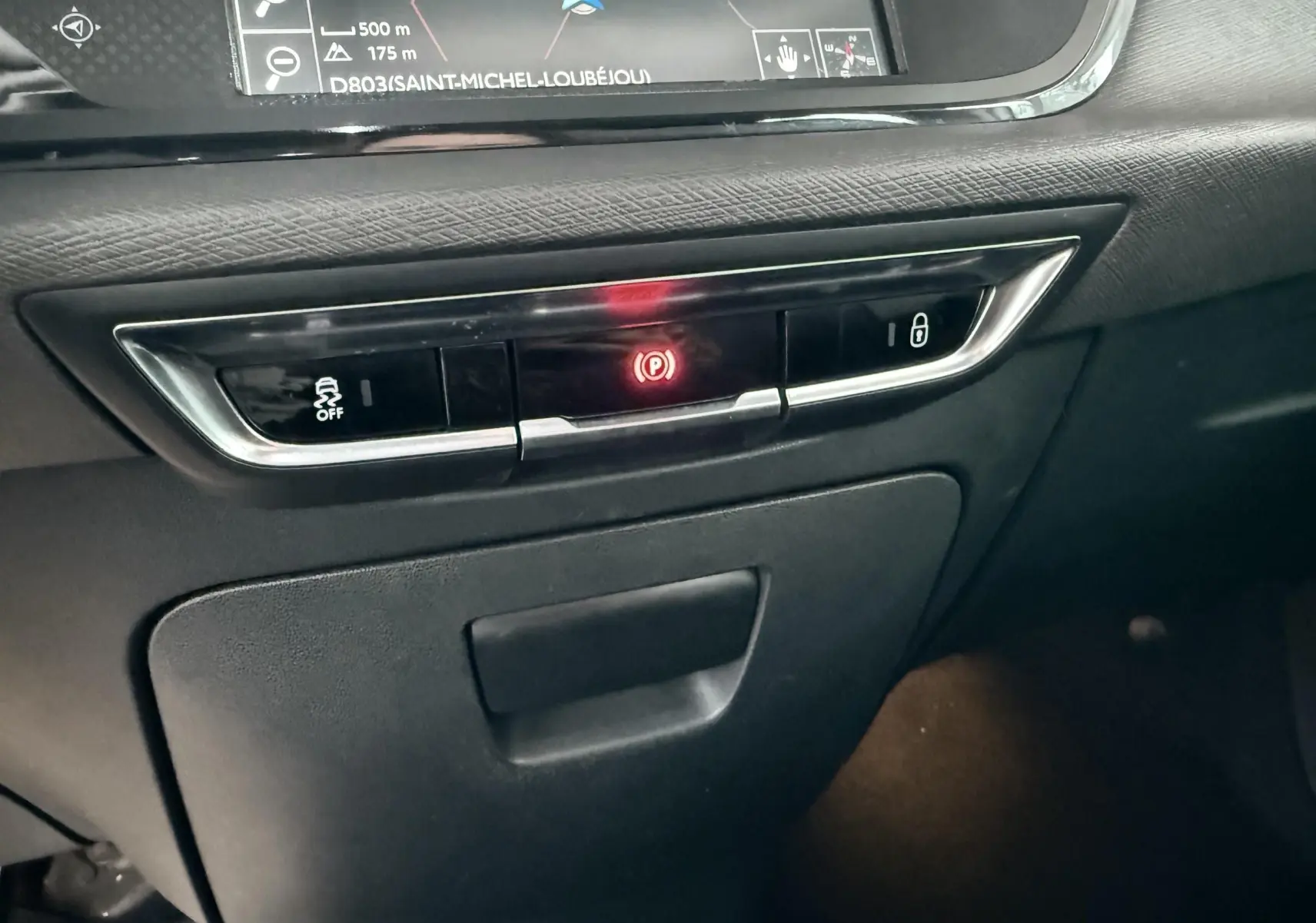 Vue rapprochée du tableau de bord central de la Citroën C4 Picasso 2015, avec bouton de frein à main électronique allumé.