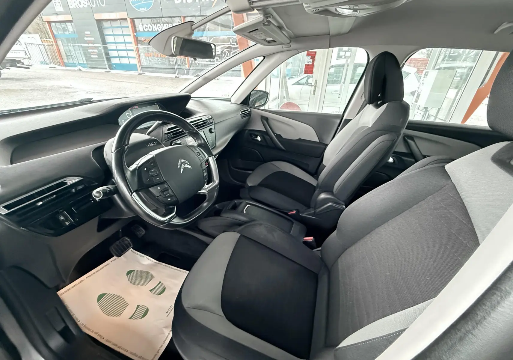 Vue intérieure côté conducteur du Citroën C4 Picasso 2015, montrant sièges tissu noir et gris et tableau de bord moderne.