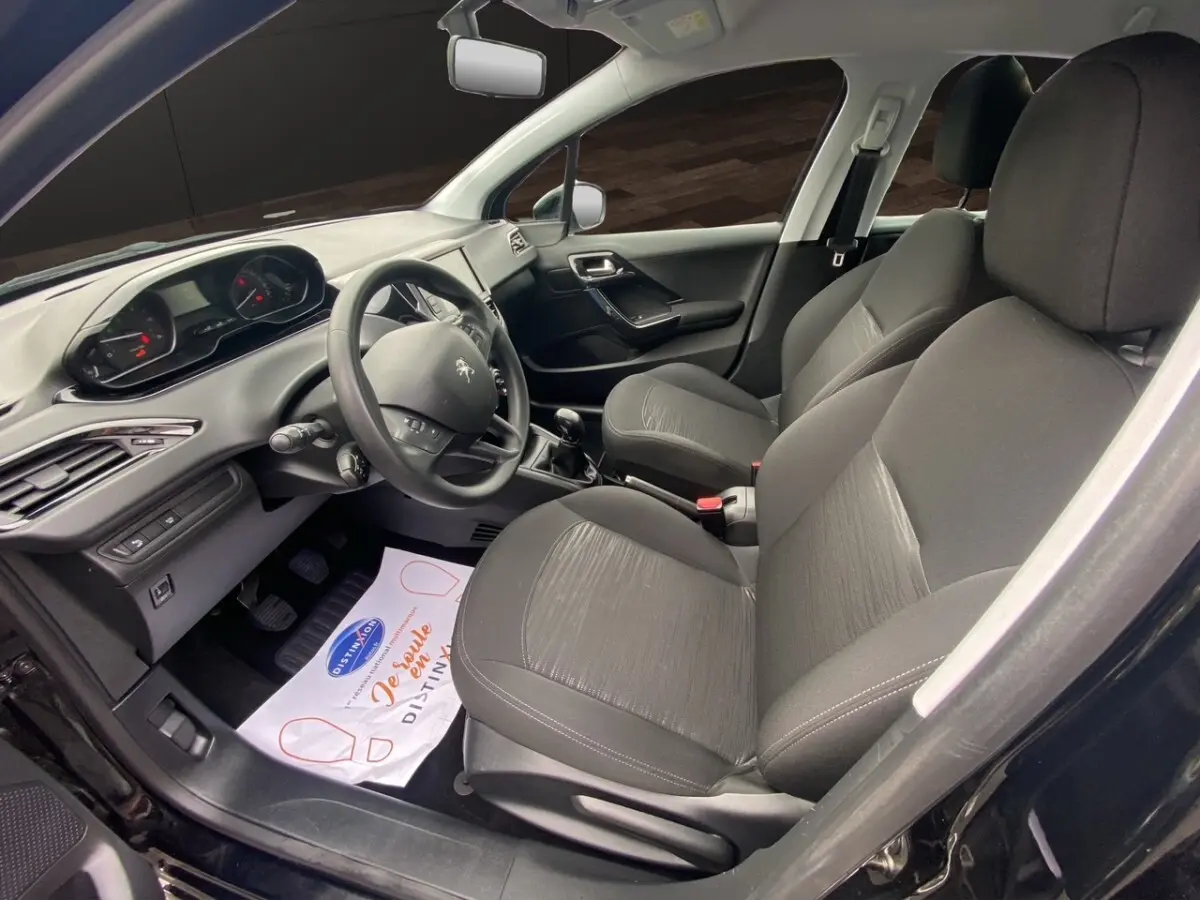 Vue intérieure côté conducteur de la Peugeot 208 Affaire noire, montrant le volant, tableau de bord et sièges tissu gris.