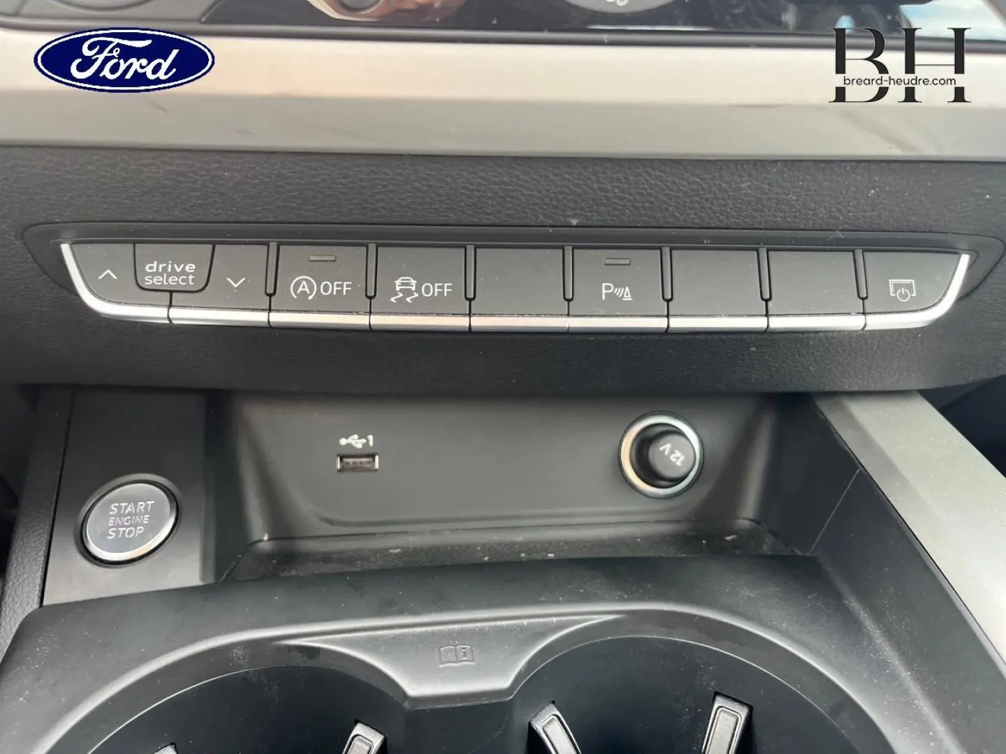 Vue rapprochée de la console centrale d'une Audi A4 Avant gris Manhattan, avec boutons de contrôle et prise 12V visibles.