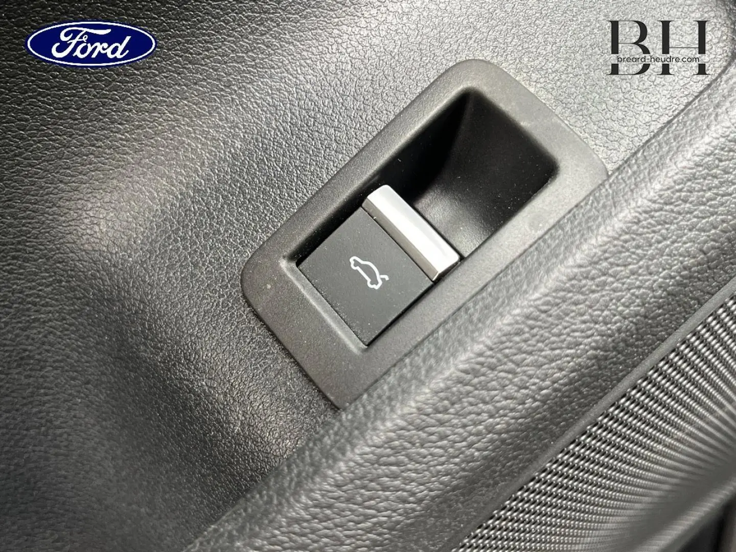 Gros plan sur le bouton d'ouverture du coffre dans l'habitacle d'une Audi A4 Avant gris Manhattan.