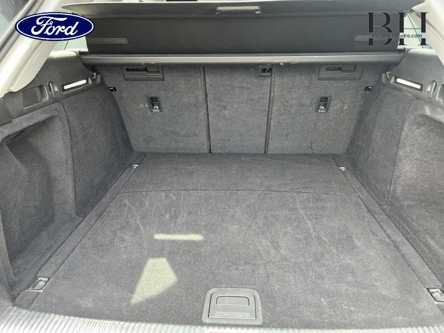 Coffre spacieux vu de l'arrière, tapis gris foncé, avec cache-bagages et fixations Isofix visibles.
