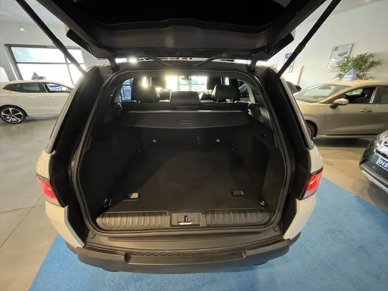 Coffre ouvert vu de l'arrière d'un Range Rover Sport blanc 2018 dans un showroom lumineux.